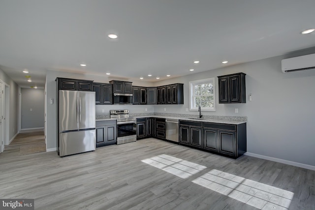 kitchen featuring sink, stainless steel appliances, a wall mounted air conditioner, light stone counters, and light hardwood / wood-style flooring