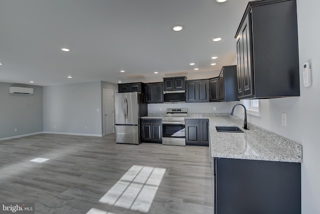 kitchen with sink, light hardwood / wood-style floors, light stone counters, stainless steel appliances, and a wall unit AC