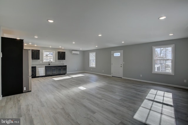 unfurnished living room featuring a wall mounted air conditioner and light hardwood / wood-style floors