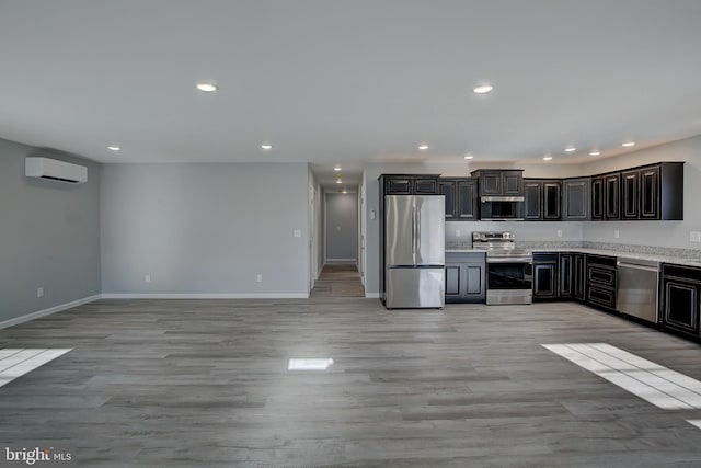 kitchen with an AC wall unit, dark brown cabinets, stainless steel appliances, and light wood-type flooring