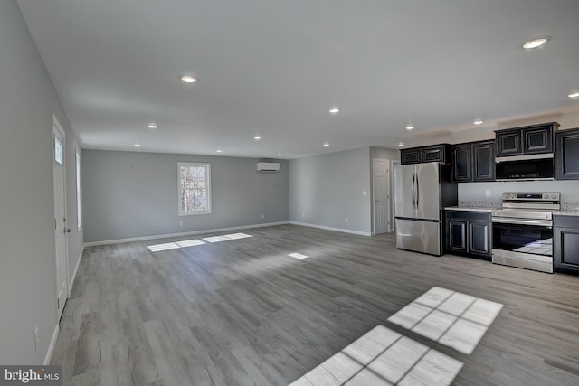 kitchen featuring light stone countertops, a wall unit AC, light wood-type flooring, and appliances with stainless steel finishes