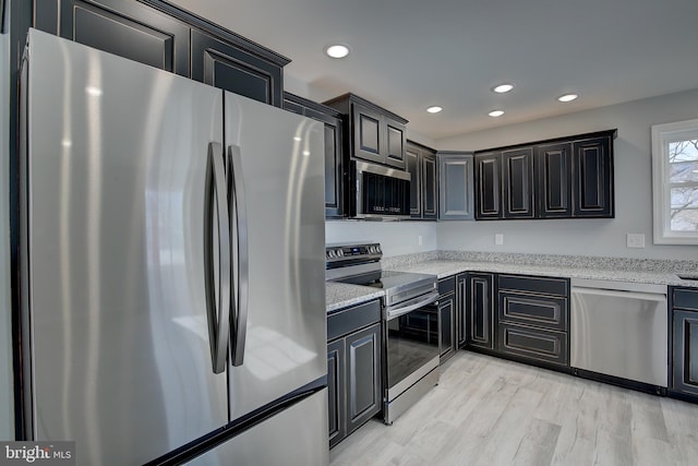 kitchen with appliances with stainless steel finishes, light wood-type flooring, and light stone counters