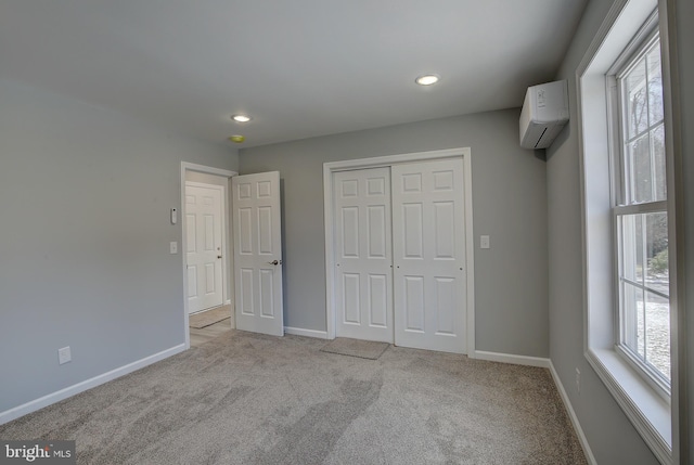 unfurnished bedroom featuring a wall unit AC, a closet, and light colored carpet