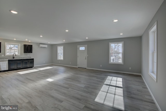 unfurnished living room with light hardwood / wood-style flooring, an AC wall unit, and sink