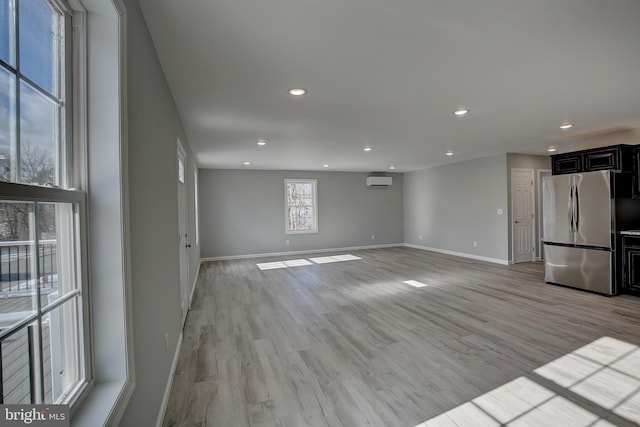 unfurnished living room featuring a wall mounted air conditioner and light hardwood / wood-style floors