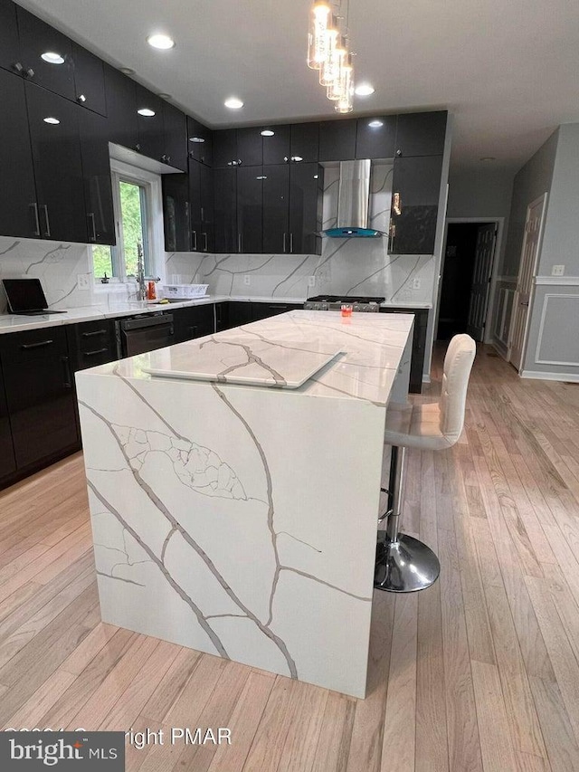 kitchen featuring a breakfast bar, wall chimney range hood, light hardwood / wood-style floors, a kitchen island, and hanging light fixtures