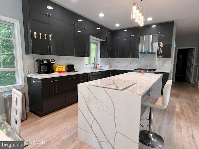 kitchen featuring wall chimney exhaust hood, light hardwood / wood-style flooring, pendant lighting, a breakfast bar area, and a kitchen island