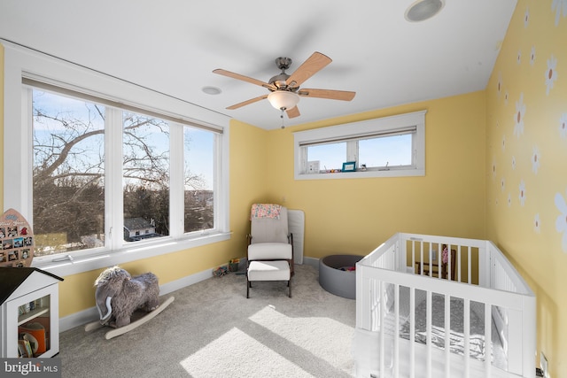 bedroom with a nursery area, light colored carpet, and ceiling fan