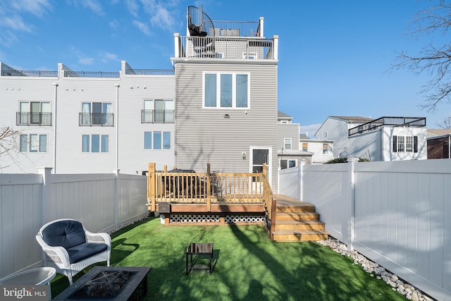 back of property with a wooden deck, a lawn, and a fire pit