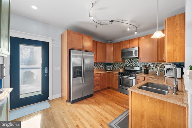 kitchen with appliances with stainless steel finishes, tasteful backsplash, sink, hanging light fixtures, and light wood-type flooring