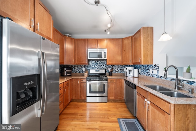 kitchen featuring appliances with stainless steel finishes, decorative light fixtures, tasteful backsplash, sink, and light hardwood / wood-style floors