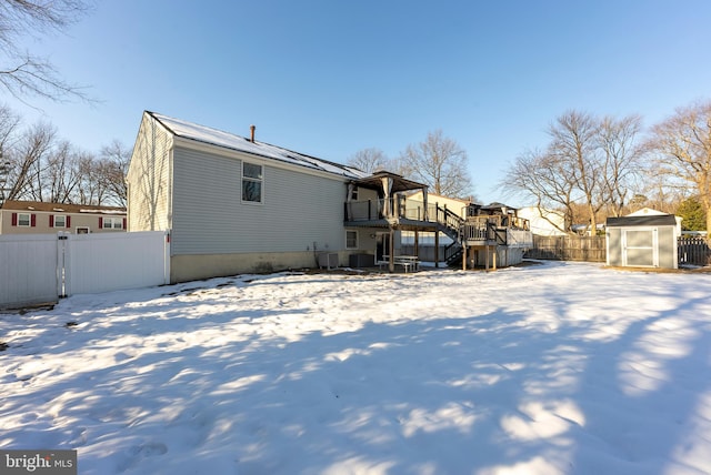 snow covered house featuring a wooden deck, a shed, and central AC unit