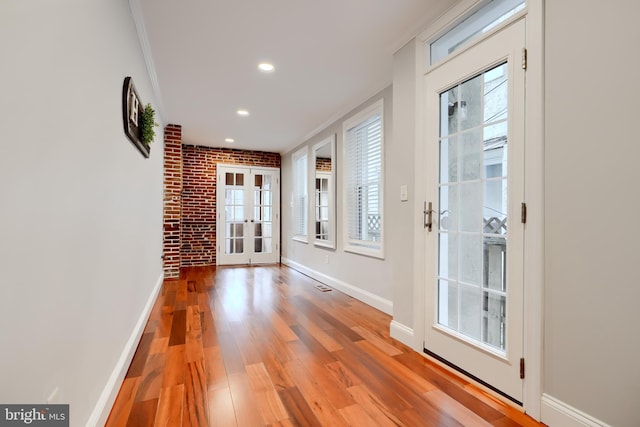 doorway with light wood-type flooring, baseboards, crown molding, and french doors