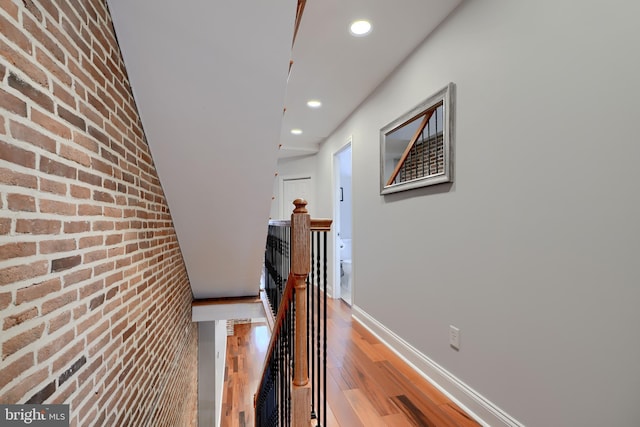 corridor with baseboards, brick wall, wood finished floors, an upstairs landing, and recessed lighting