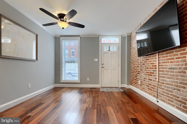 entryway with wood-type flooring, ornamental molding, ceiling fan, brick wall, and baseboards