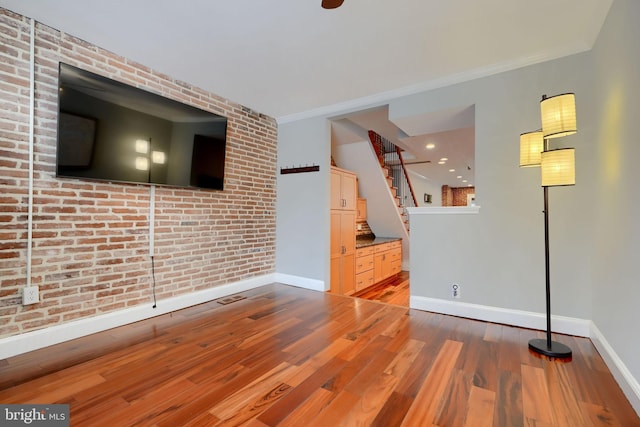 spare room featuring brick wall, baseboards, wood finished floors, and ornamental molding