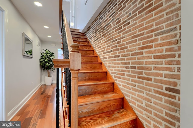 stairway featuring brick wall, recessed lighting, wood finished floors, and baseboards