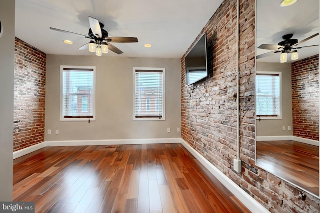 spare room featuring brick wall, wood-type flooring, and baseboards