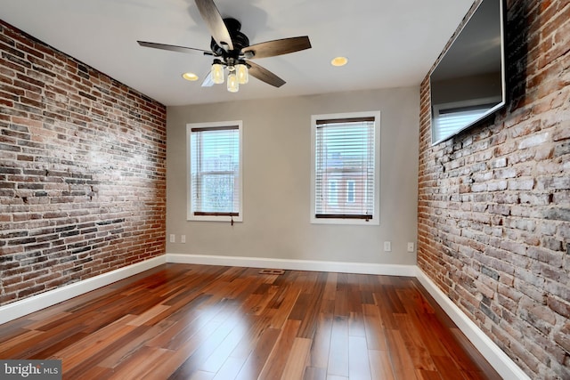 empty room with brick wall, baseboards, and hardwood / wood-style floors