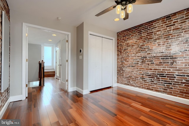 unfurnished bedroom with brick wall, a closet, baseboards, and wood finished floors