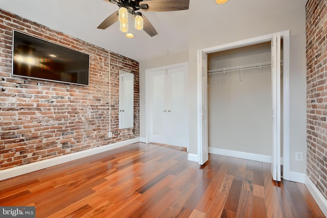 unfurnished bedroom with baseboards, ceiling fan, brick wall, and wood finished floors