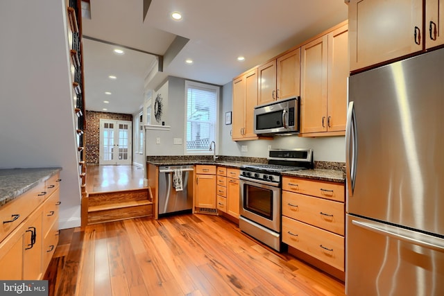 kitchen featuring stainless steel appliances, light brown cabinets, a sink, and light wood finished floors