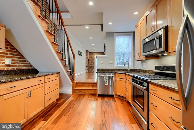 kitchen featuring dark stone counters, appliances with stainless steel finishes, light wood finished floors, and a sink