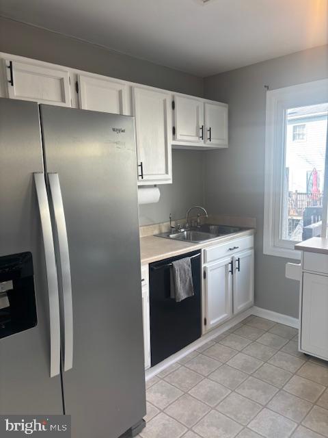 kitchen featuring light tile patterned floors, sink, stainless steel fridge, black dishwasher, and white cabinets