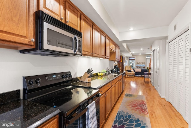 kitchen with dark stone counters, stainless steel appliances, light hardwood / wood-style floors, and sink