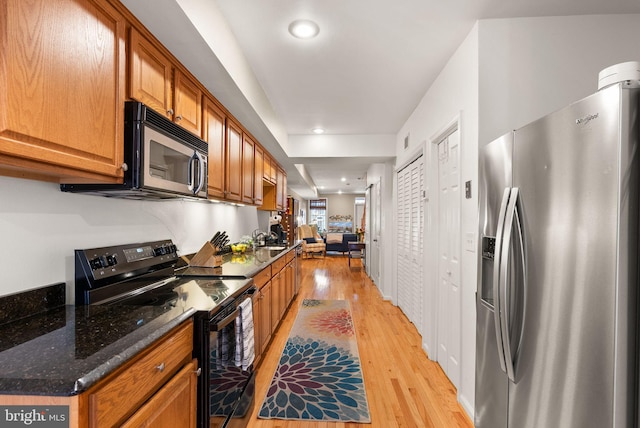 kitchen featuring stainless steel appliances, sink, light wood-type flooring, and dark stone counters