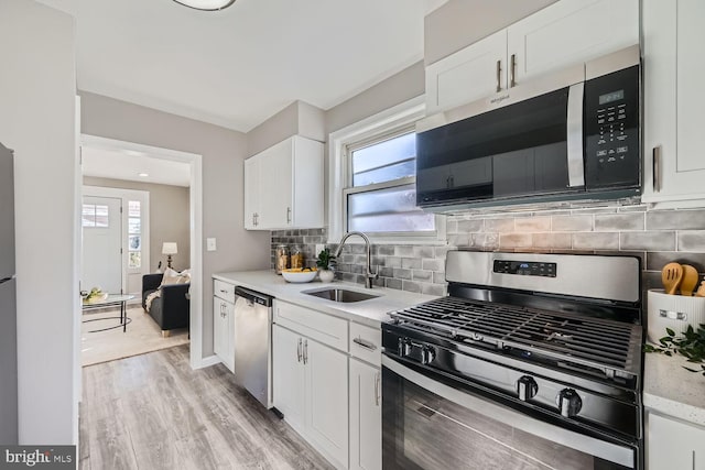 kitchen featuring white cabinets, stainless steel appliances, sink, light hardwood / wood-style flooring, and backsplash