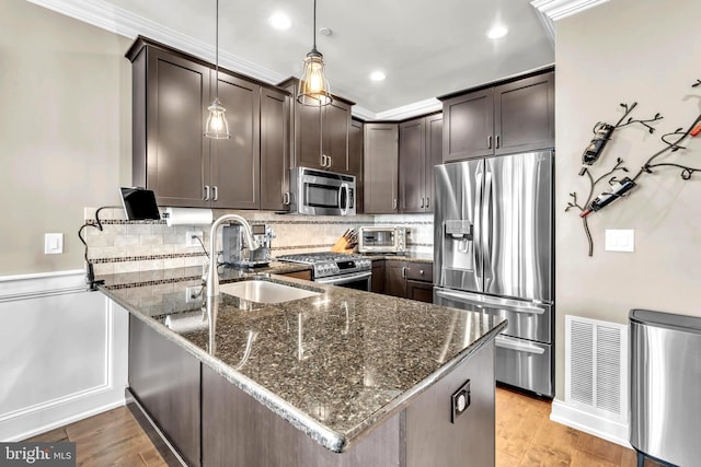 kitchen featuring dark brown cabinets, dark stone countertops, ornamental molding, pendant lighting, and stainless steel appliances