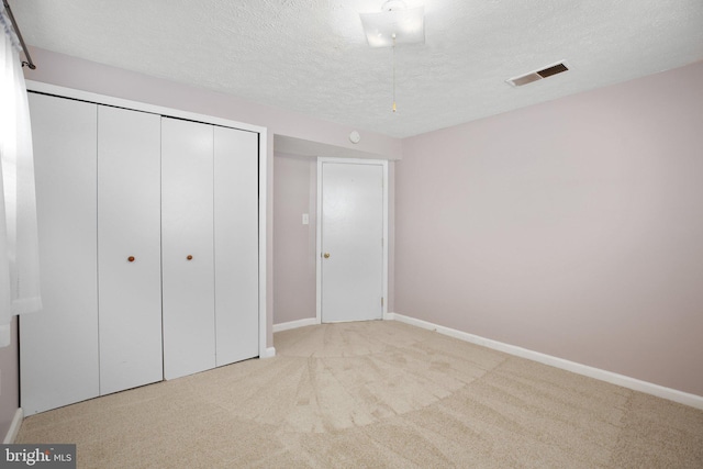 unfurnished bedroom featuring light carpet, a textured ceiling, and a closet