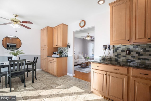 kitchen with dark stone countertops, light tile patterned floors, decorative backsplash, and ceiling fan