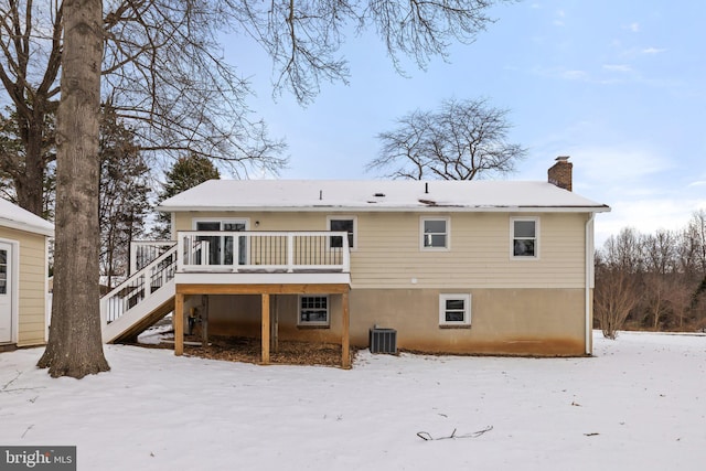 snow covered back of property with central AC unit and a wooden deck