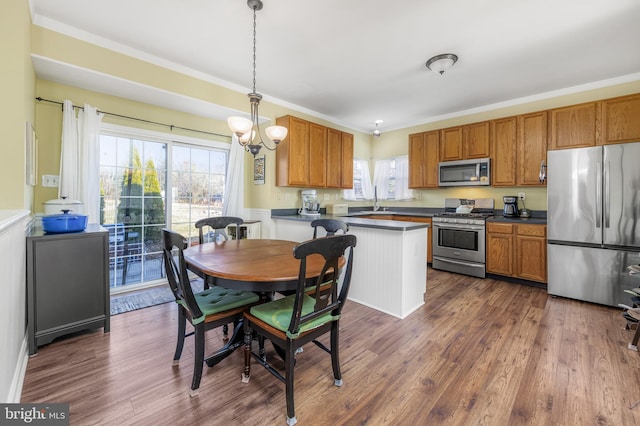 kitchen with ornamental molding, dark wood-type flooring, decorative light fixtures, and appliances with stainless steel finishes