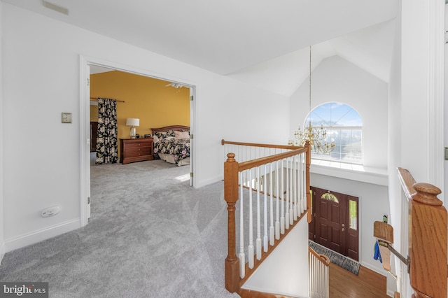 hallway with light carpet, a chandelier, and vaulted ceiling