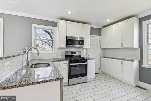 kitchen featuring appliances with stainless steel finishes, white cabinets, a sink, and dark stone countertops