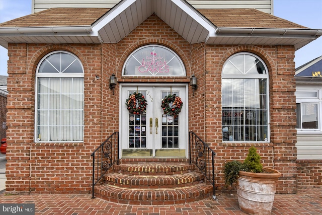 property entrance with french doors, roof with shingles, and brick siding