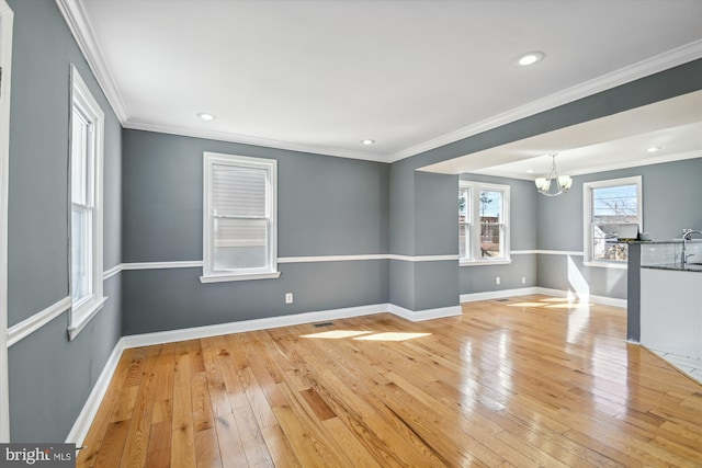 spare room featuring a chandelier, ornamental molding, light wood-style flooring, and baseboards