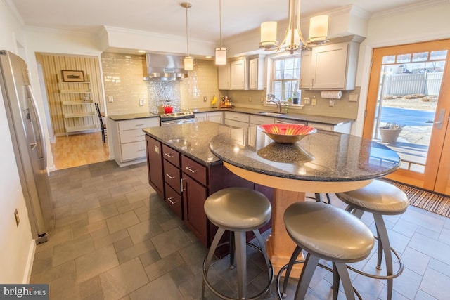 kitchen featuring wall chimney exhaust hood, stainless steel appliances, white cabinets, pendant lighting, and a center island