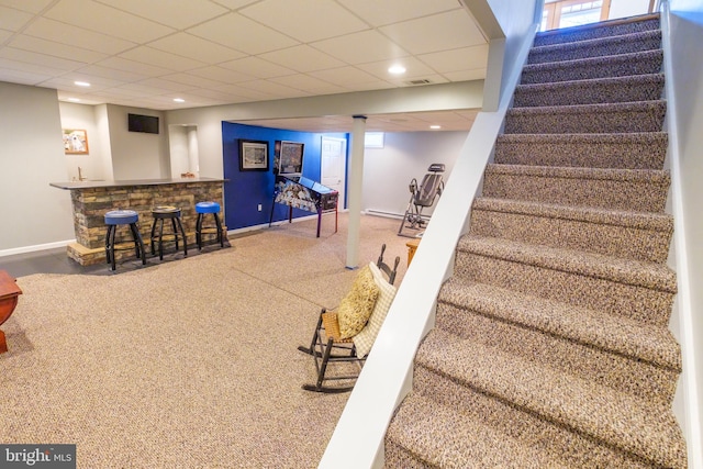 interior space featuring a paneled ceiling, carpet floors, and bar area