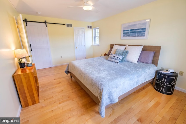 bedroom featuring light wood-type flooring, ceiling fan, and a barn door