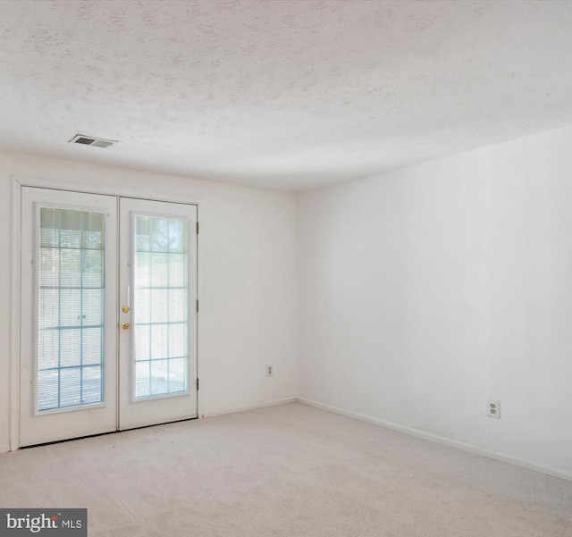 carpeted empty room with a textured ceiling and french doors