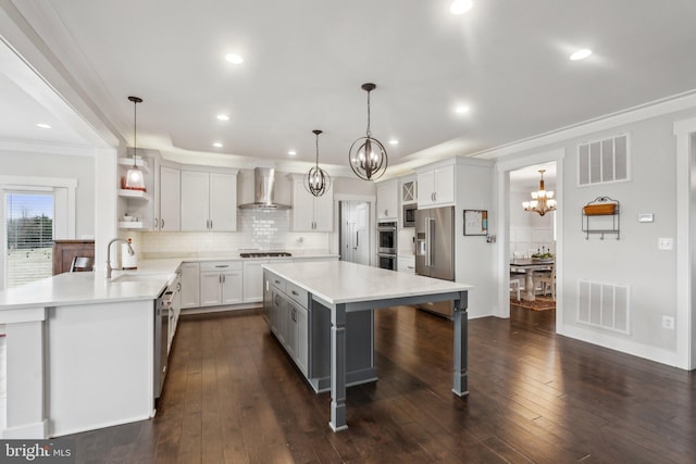 kitchen with sink, a breakfast bar area, a chandelier, hanging light fixtures, and wall chimney range hood