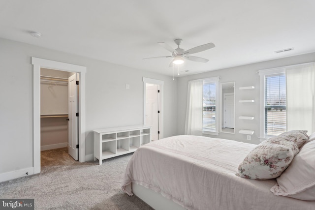 bedroom with ceiling fan, a walk in closet, carpet flooring, and multiple windows