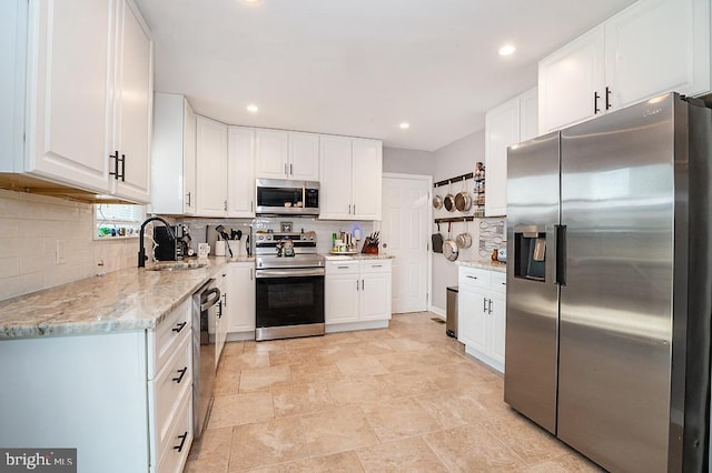 kitchen featuring light stone countertops, sink, decorative backsplash, white cabinets, and appliances with stainless steel finishes