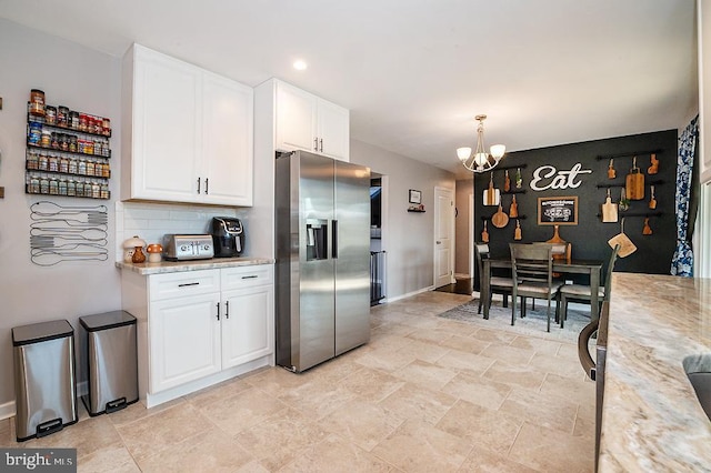 kitchen featuring light stone countertops, stainless steel fridge, decorative light fixtures, an inviting chandelier, and white cabinetry