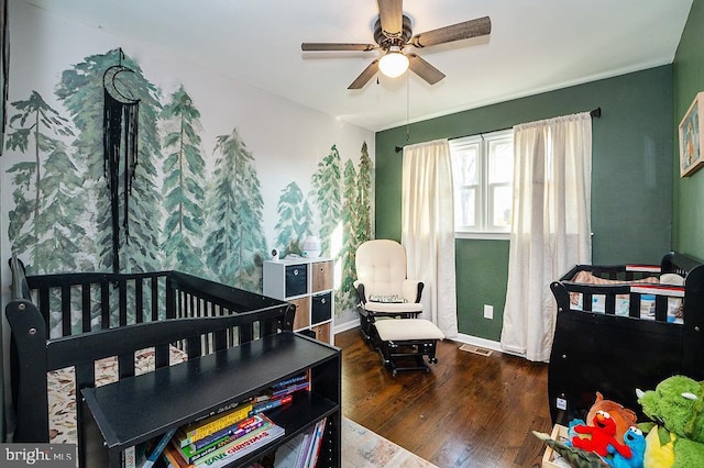 bedroom featuring dark hardwood / wood-style floors, a nursery area, and ceiling fan