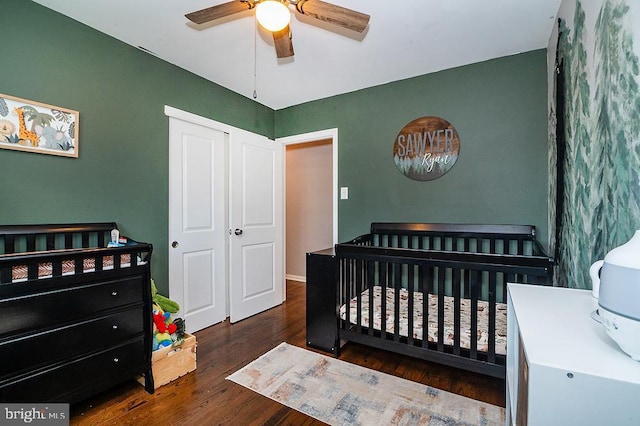 bedroom with ceiling fan, dark wood-type flooring, and a nursery area